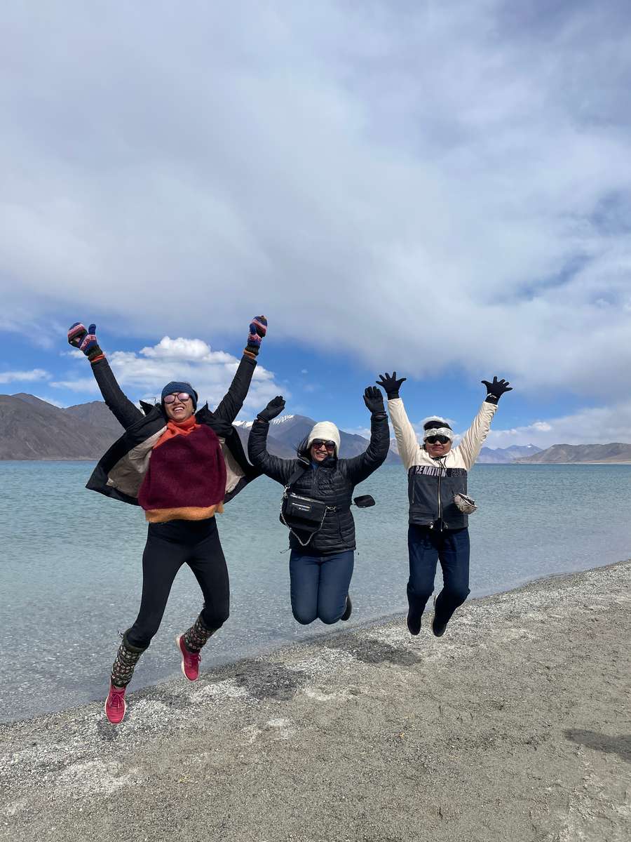 Three travellers jumping for joy on a Ladakh hillside